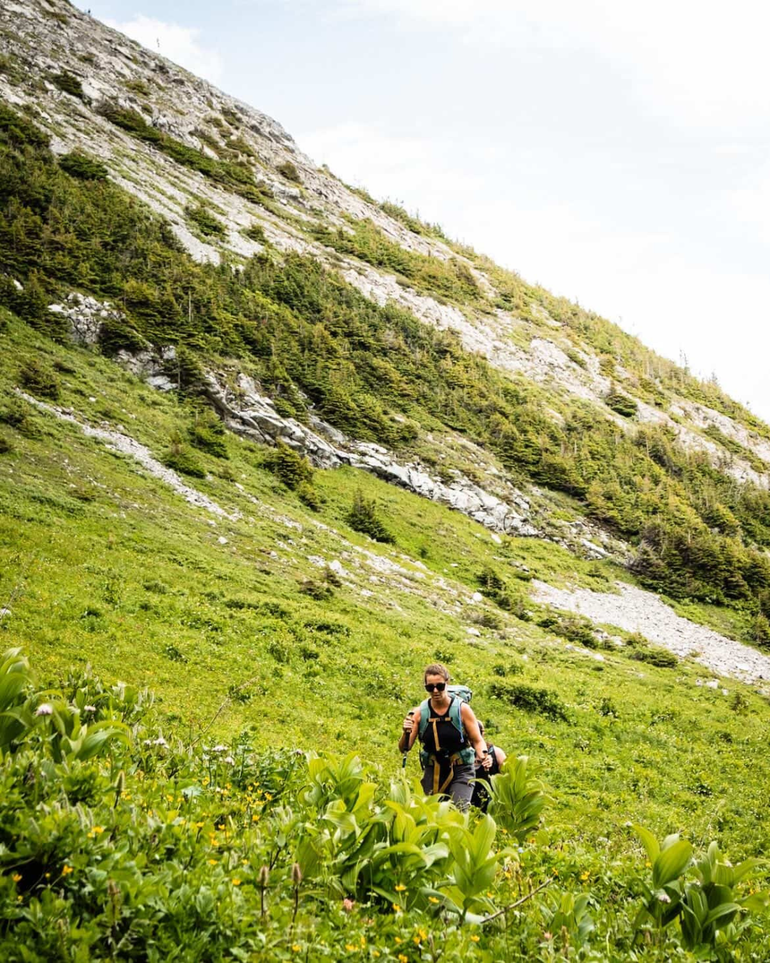 Woman backpacking up steep meadow slope — Court Jacobs